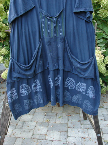 A navy Barclay Farmer Jen Tunic Dress with a shell flower theme paint on the front and back. It has a rear elastic tab, oversized bushel front drop pockets, and a lower bell shape with a deeper rounded neckline. Made from organic cotton, it measures 45 inches in length with bust, waist, and hip measurements of 56, 60, and 66 respectively.