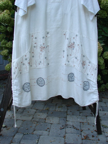 Image alt text: Barclay Linen Farmer Jen Dress Daisy Days Natural Size 2 - White sheet dress with a design, cotton sleeves, and a paneled lower hem.