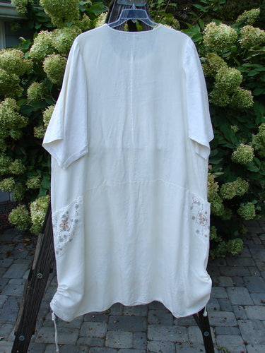 A white Barclay Linen Farmer Jen Dress with a floral design, featuring a sectional bodice, wrap around pockets, and cotton three-quarter length sleeves with lettuce edgings. The dress has a significant A-line flair and sports the Daisy Day theme paint. Perfect condition. Size 2.