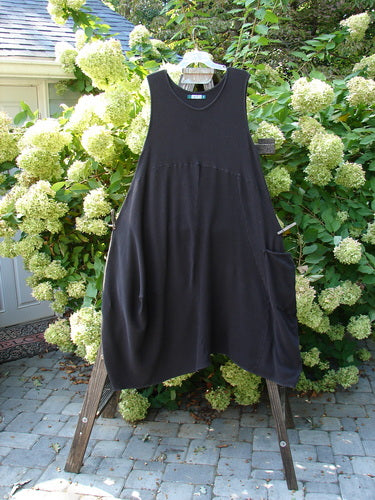 A Barclay Thermal 4 Square Tulip Jumper in Storm, a black dress on a rack, with a cozy ribbed thermal waffle and lower rib combination, a drop downward scooped slight empire waistline, a huge pocketed lower bell shape, and belled and varying hemline.