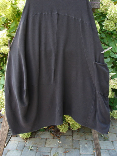 A black skirt with a pocket on a clothes rack, part of the Barclay Thermal 4 Square Tulip Jumper in Storm. Made from cotton thermal, this cozy ribbed waffle skirt features a drop downward scooped slight empire waistline, a huge pocketed lower bell shape, and additional S curved seams. The skirt has a belled and varying hemline, deeper arm openings, and an oval neckline. Bust: 50 (open), waist: 50, hips: 56, long length: 53, shorter length: 50 inches.