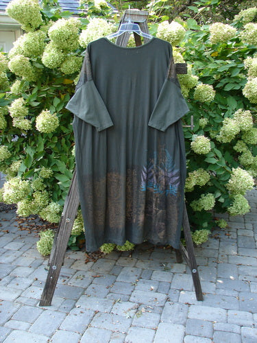 The Barclay Bamboo Drop Pocket Dress with Metallic Medallions in Black Sand OSFA hangs elegantly on a wooden rack, showcasing its unique boatneck, contrasting sleeves, and dynamic pocket design.