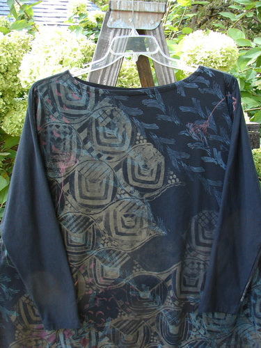 A Barclay Cotton Lycra Treesoul Top in Black, featuring a wide square flair and a boatneck rolled neckline. The top is shown on a clothes rack, with a close-up of a bush in the background.