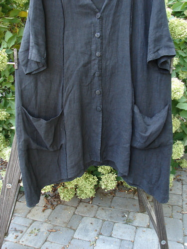 A black linen jacket with double tie back and front drop flop pockets. Features a deep V-shaped neckline, exterior vertical stitchery, and a varying hemline. Size 1.