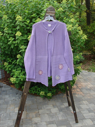 Image: A purple sweater on a swinger, with a pair of purple towels on a wooden ladder in the background.

Alt text: 1999 Rollneck Cardigan Sweater Pinwheel Viola OSFA - A purple sweater hanging on a swinger, with towels on a wooden ladder.
