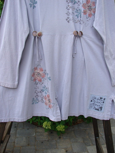 2000 4 Vent Top Daisy Grid Pale Purple Size 1: A white shirt with flowers on it, featuring a V-shaped neckline and sectional floral paint. Accented with rippie buttons and 4 unique vents. A sweet front pocket completes the look.