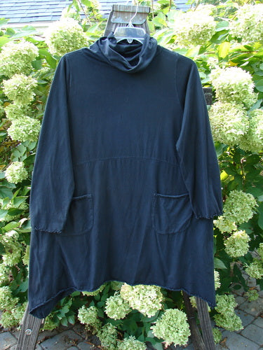 Image alt text: Barclay Cowl Neck Double Pocket Curl Edge Tunic Top, a black mid-weight organic cotton shirt on a swinger, with a curly edged flop turtleneck, drop front exterior pockets, and sweet lettuce edgings.