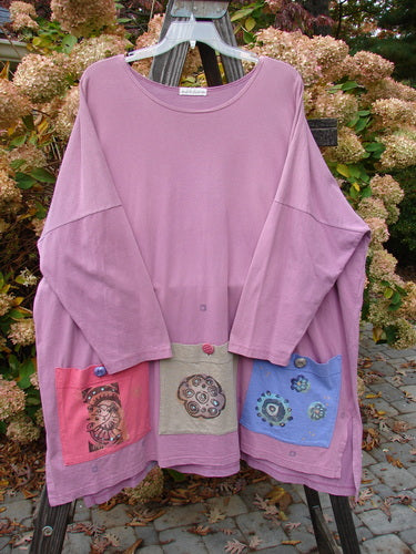 1997 Collage Top Petal Power Crocus OSFA: A pink shirt with different designs on a clothes rack. Features include an A-lined shape, drop shoulders, vented sides, and oversized front pockets with vintage knot buttons.