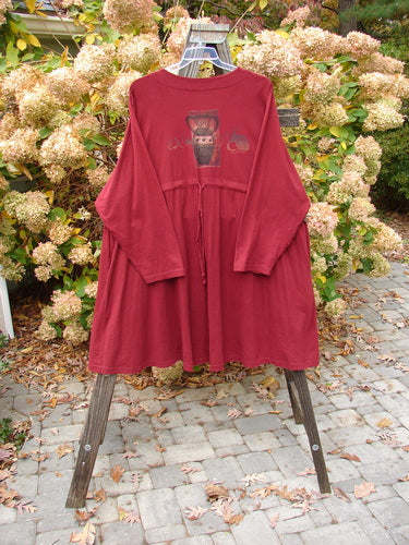 A red shirt with a picture on it, hanging on a rack. 1997 Mask Jacket Primitive Vase Regalia Size 2.