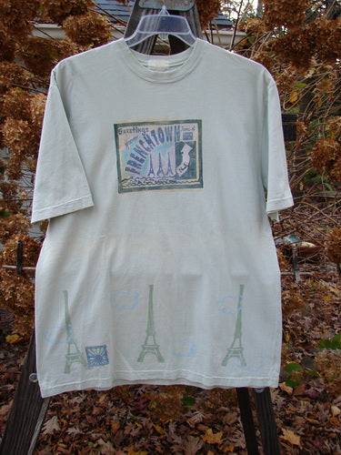 A white short-sleeved tee with a graphic design featuring a postcard theme of Frenchtown. Made from organic cotton jersey. Size 1.