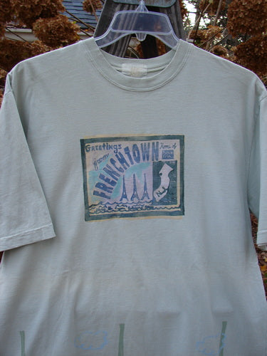 2000 Short Sleeved Tee Greetings from Frenchtown Dune Grass Size 1: A white shirt with a picture of a postcard theme paint and a Blue Fish patch.