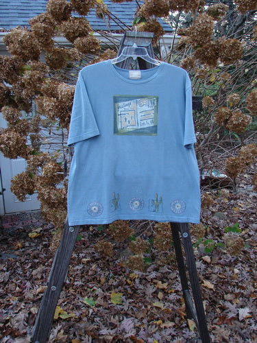 2000 Short Sleeved Tee Greetings from Santa Fe Blue Jet Size 1: A blue tee with a postcard theme paint and Blue Fish patch.