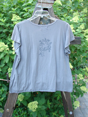 Image alt text: Barclay Batiste Cap Sleeved Top Night Bird Storm Grey Size 1, a grey shirt on a wooden rack, featuring a slight A-line flair and sweet cap sleeves.