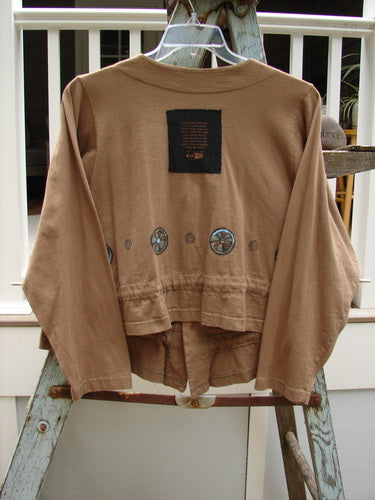 1997 Treehouse Jacket Tiny Pinwheel Portico Size 1: A brown jacket with a patch on it, featuring a double paneled V neck, button line, and drawcord flounce.
