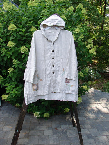 1998 Traveler's Jacket, white linen coat on a stand, with corded linen flyaway hoodie, full front button, vented sides, deep side pockets, square lower hem, celestial travel theme paint, Blue Fish patch.