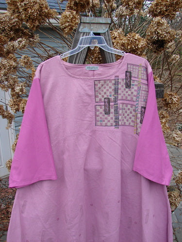 A Barclay Cotton Sleeve Hemp Linen Sectional Dress in Rose, featuring a pink shirt with a pattern on it. The dress has a sectional upper with a downward curved empire waist seam, a varying and pleated A-line shape, and a slightly shallow rounded neckline. The contrasting cotton three-quarter length sleeves add a unique touch. Perfect for a vintage Blue Fish Clothing collection.