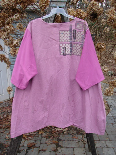 A Barclay Cotton Sleeve Hemp Linen Sectional Dress in Rose, featuring a pink shirt with a patchwork design and contrasting cotton three-quarter length sleeves. The dress has a sectional upper with a downward curved empire waist seam and a slightly shallow rounded neckline. The image shows a close-up of the dress, highlighting the fabric and design details.