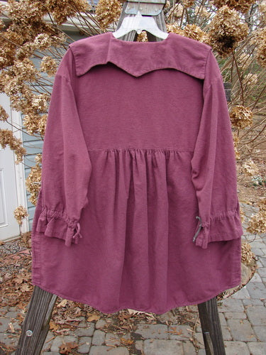 2000 Flannel Poet's Top Spin City Murple Size 2: A close-up of a purple shirt on a wooden pole. Uniquely styled jester's collar, rounded vented hemline, mix-matched pull cord lower sleeves, oversized angled front pockets, and tons of tiny original buttons.