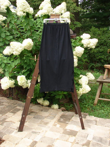 1993 Tie Skirt Unpainted Black Size 1: A black pants on a clothes rack, with a person wearing a black robe.