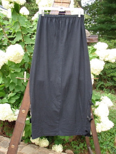 1993 Tie Skirt Unpainted Black Size 1: A black skirt on a wooden rack. Full elastic waistline, slightly pegged and vented. Accented with short velvet side ties.