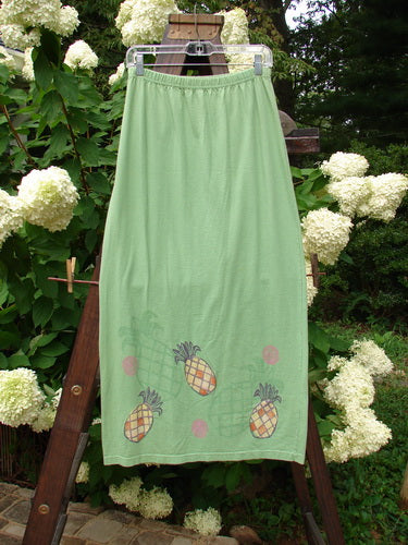 1999 Straight Skirt Pineapple Spearmint Size 0: A skirt on a rack with a green dress and towel featuring pineapple designs, and a close-up of a white flower.
