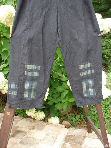 Image alt text: "2000 Waveline Pant Grid Block Black Size 2: A pair of pants with patches on a clothesline, made from light weight hemp. Unique flat button front waistline with a full elastic back. Slight crop length with a generous hip measurement. Supreme big block grid theme paint and a nice drape. Waist fully relaxed 34, waist extended 48, hips 48, inseam 25, length 40 inches."