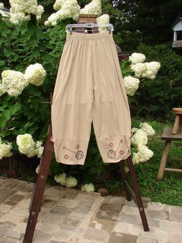 Image alt text: 1996 Boulevard Pant Star Travel Dune Size 1 - A pair of pants on a rack, featuring a two-inch elastic waistline, side seam pockets, and overlapping painted cuffs with cloth covered buttons. Made from organic cotton, these pants have a slightly shorter rise and a star travel theme paint.