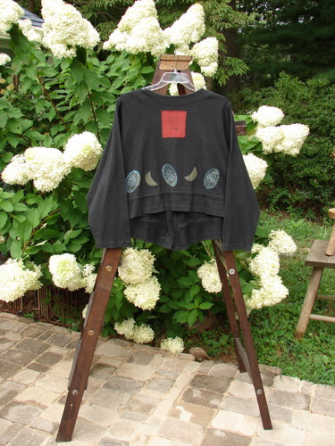 1997 Treehouse Jacket Many Moons Cast Iron Size 2: A black shirt with a design on it, featuring a stone walkway with white flowers in the background.