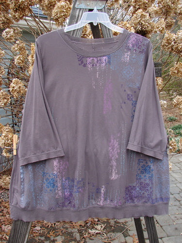 Image: A long sleeved shirt on a clothes rack. The shirt is purple with blue and purple designs. There is a close-up of the fabric, showing a purple and blue pattern. The shirt is part of the Barclay Flutter Net A Lined Tee Top Perimeter Mushroom Size 2 collection. 

Alt text: "Barclay Flutter Net A Lined Tee Top Perimeter Mushroom Size 2: Long sleeved purple shirt with blue and purple designs on a clothes rack."