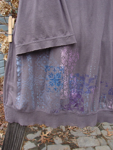 A close-up of the Barclay Flutter Net A Lined Tee Top Perimeter Mushroom Size 2, a purple and blue shirt with netted flutter details on the neckline and sleeves. Made from mid-weight organic cotton, this three-quarter sleeved shirt features a significant perimeter theme paint design on the lower hem. Bust 50 ~ Waist 52 ~ Hips 58 ~ Sweep 68. Length: 31 inches.