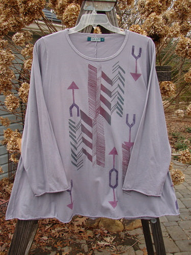 Image: A long sleeved shirt on a swinger with arrows on it.

Alt text: Barclay Long Sleeved A Lined Tee Top Arrow Mottled Lavender Size 2, swinging on a swinger.
