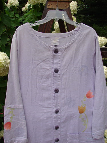 2000 Woven Hemp Sophia Cardigan Tulip Lilac Size 1: A purple shirt with flowers on it, featuring a rounded neckline, front button closure, drop pocket, and ripple sleeve accent. Made from textured woven hemp cotton.