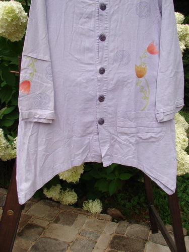 2000 Woven Hemp Sophia Cardigan Tulip Lilac Size 1: A white shirt with flowers on it, featuring a rounded neckline, front button closure, drop pocket, and ripple sleeve accent. Made from textured woven hemp cotton, this cardigan is from the Spring Collection of 2000.