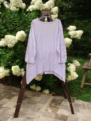 2000 Woven Hemp Sophia Cardigan Tulip Lilac Size 1: A white shirt on a clothes rack, featuring a rounded neckline, front button closure, drop pocket, and ripple sleeve accent. Made from textured woven hemp cotton.