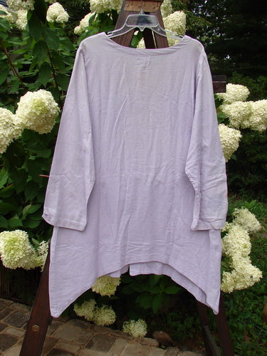 2000 Woven Hemp Sophia Cardigan Tulip Lilac Size 1: A long-sleeved shirt on a clothesline, with a close-up of flowers and leaves.