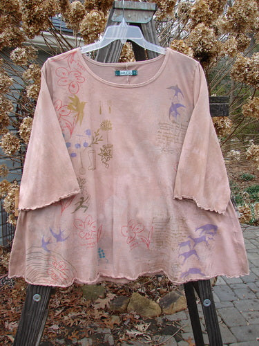 A Barclay Three Quarter Sleeved Crop A Lined Tee Top in Mottled Mauve, featuring a pink shirt with drawings and designs on it.