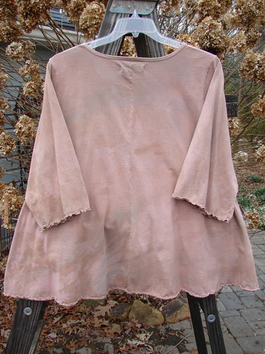 A pink shirt with three-quarter sleeves and a rounded neckline, featuring sweet curly edgings. The shirt is on a wooden rack.