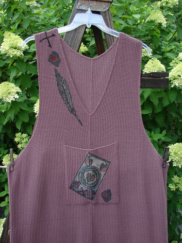 A 1993 Waffle Pocket Sweater Jumper in Dusty Plum, featuring a purple vest with a feather and a black and red design. The jumper has an oversized front painted pocket with a vintage button, a plunging V neckline, and a heart feather theme paint. Made from thick thermal waffle weave, it has a great weight and texture. Bust 20 and Open, Waist 54, Hips 54, Arm Opening Length 19, and Length 53 Inches. Perfect for collectors of vintage Blue Fish Clothing.
