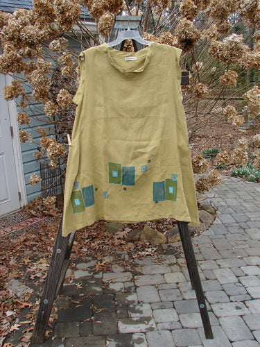 Barclay Linen Mid Layer Cap Sleeve Tunic Geometric Mustard Size 2: A yellow shirt with blue squares on a rack, featuring a varying widening hemline, downward curved front and rear drop empire waist seam, and a mock mandarin collar.