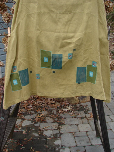Barclay Linen Mid Layer Cap Sleeve Tunic in Mustard, featuring a cloth on a clothesline. Varying widening hemline, downward curved front and rear drop empire waist seam, mock mandarin collar, and continuous geometric theme paint. Size 2.