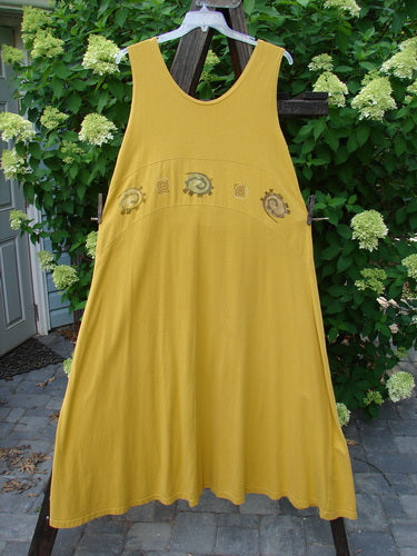 1995 Zelda Jumper Dress Abstract Key Lemon Size 2: A yellow dress with a sweeping A-line shape, featuring a rounded neckline and a waist seam. The dress is hanging on a clothesline in an outdoor setting.