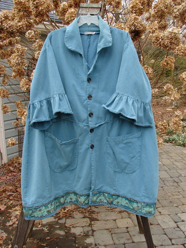 A Barclay Decora Brushed Twill Flutter Coat in Peacock, size 2. A blue coat with ruffles, made from heavy brushed cotton twill. Features include a deep V-shaped neckline, matching buttons, and flutter ruffle 3/4 length sleeves. With a paneled and widening swingy hemline, this coat is painted in the vine garden theme. Bust: 60, Waist: 60, Hips: 62, Sweep: 75, Lower Bell: 80, Length: 46 inches.