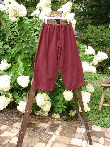 Image: A pair of pants on a rack. The 1999 Flannel PJ Pant Pom Pom Unpainted Wine Size 0 from Bluefishfinder.com. Heavyweight flannel with a shorter rise, drawcord front waistline, and elastic backing. Crop length with pom poms around each cuff. Waist 28 relaxed, waist expanded 48, hips 46, inseam 22, length 32 inches.