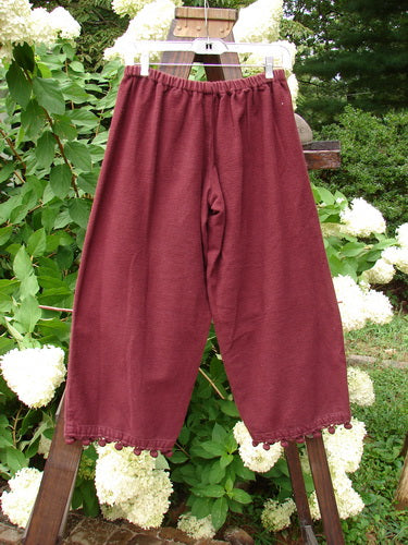 1999 Flannel PJ Pant Pom Pom Unpainted Wine Size 0: A pair of pants on a clothes rack, made from heavy weight flannel. Crop length with pom poms around each cuff.