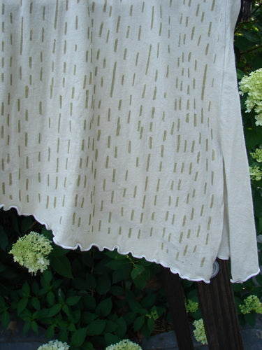 A white cloth on a clothesline, featuring a Barclay Batiste Curly Seam Tank in Sand. Featherweight cotton batiste with curly edgings, asymmetrical lower vented hem, and rain theme paint. Size 2.