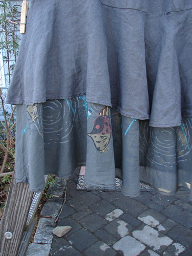 Image alt text: Barclay Linen Two Tier Ruffle Skirt with Angel Fish design, Storm Grey, Size 2. A grey skirt with a face on it, featuring a fish drawing.