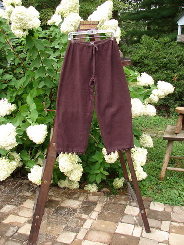 1999 Flannel PJ Pant Pom Pom Unpainted Deep Burgundy Size 0: A pair of pants on a rack with a shorter rise, draw cord front waistline, and crop length. Made from heavy weight flannel, featuring pom poms around each cuff.