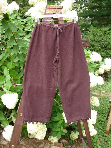 1999 Flannel PJ Pant Pom Pom Unpainted Deep Burgundy Size 0: A pair of pants on a clothesline with pom poms around each cuff.