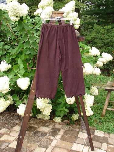 1999 Flannel PJ Pant Pom Pom Unpainted Deep Burgundy Size 0: A pair of pants on a rack, made from heavy weight flannel. Crop length with pom poms around each cuff.