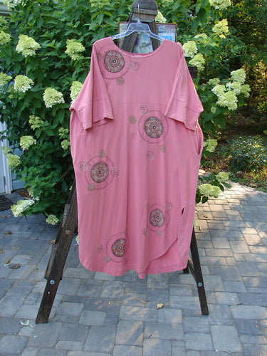 Barclay Naiad Dress Medallion Glow Size 2: A pink dress on a rack with a patterned shirt. Features a tapered shape, generous bust, rear draw cord, and shorter sleeves. Rounded hemline, deep side pockets, and Barclay Medallion paint. Bust 60, waist 60, hips 60, length 54 inches.